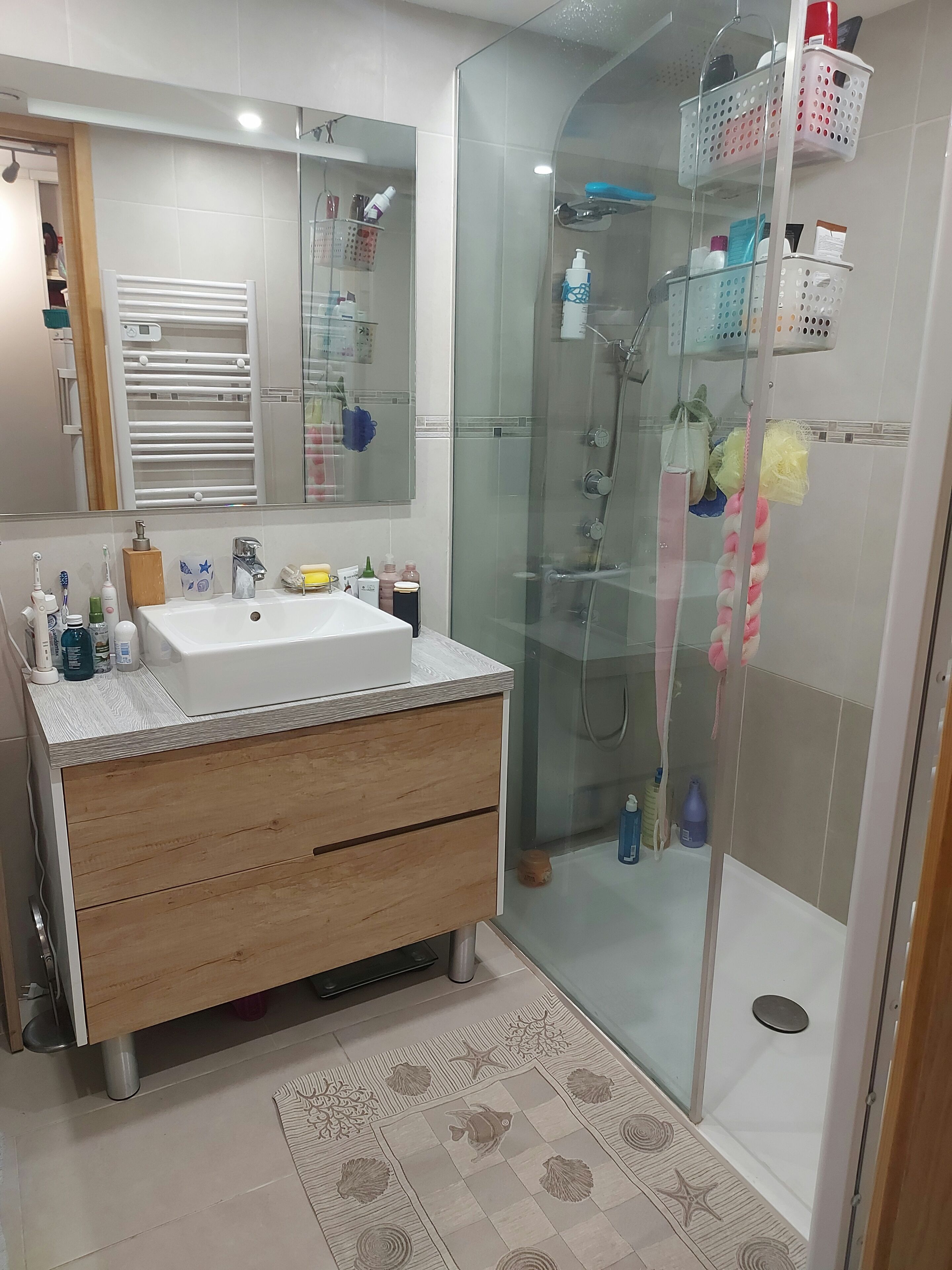 A modern bathroom with a large mirror, a sink, a shower, and a glass-enclosed shower area.