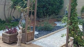 Une structure de pergola en bois, ornée de plantes grimpantes, d’une statue et d’un parterre fleuri avec des plantes rouges.