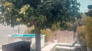 Un jardin avec une piscine, un arbre, un espace barbecue et un potager clôturé.