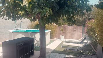 Un giardino sul retro con piscina, un albero, area barbecue e giardino recintato.