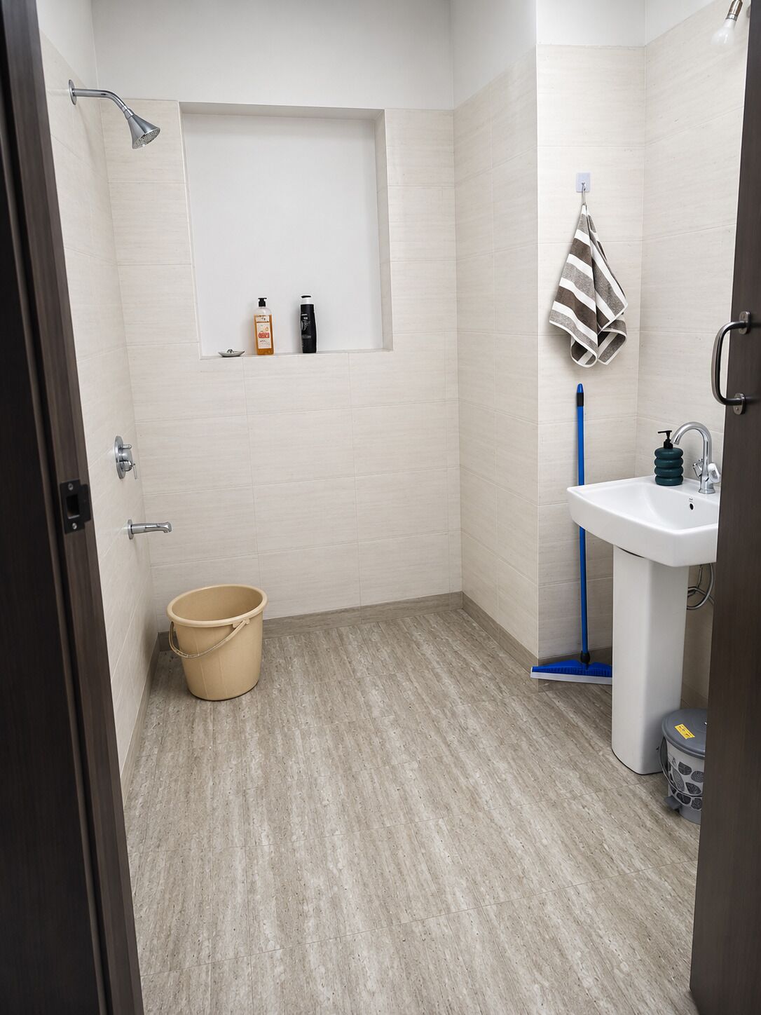 Ein Badezimmer mit Dusche, Waschbecken, Handtuchhalter und einem Eimer.
