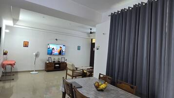Ein Essbereich mit Tisch, Stühlen, einem Ventilator und einem Fernseher im Hintergrund.