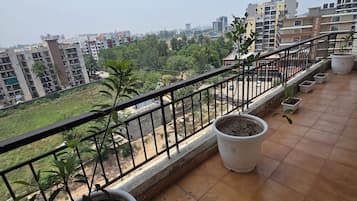 Ein Balkon mit Blumentöpfen, Fliesenboden und Blick auf umliegende Gebäude und Grünflächen.