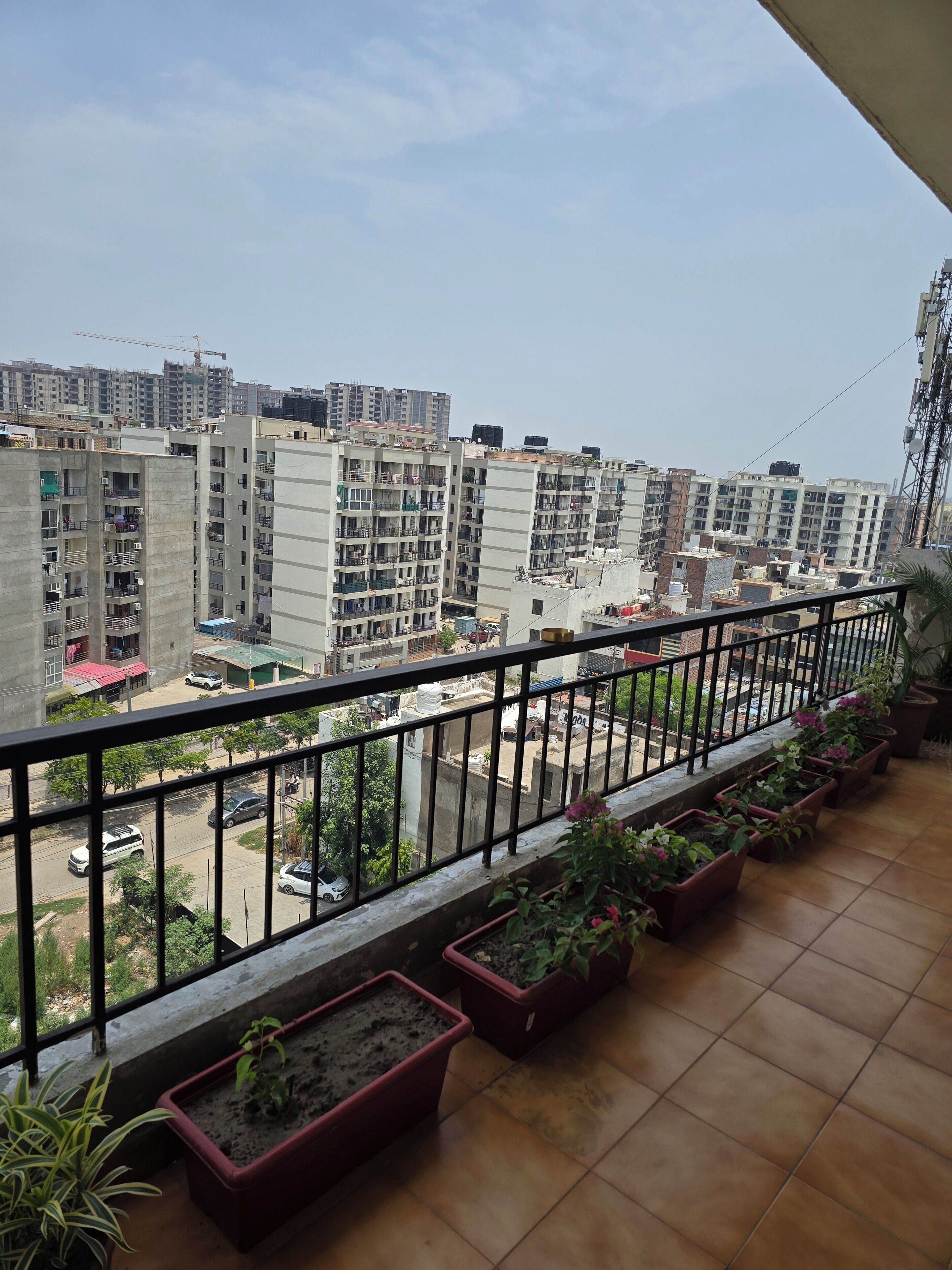 Ein Balkon mit Blumentöpfen, Fliesenboden und Blick auf umliegende Gebäude.