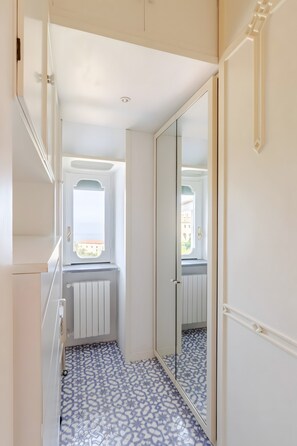 A narrow hallway with patterned flooring, a mirrored closet door, and a window with a view of buildings. - Holiday Home 'Alexandra' with Sea View, Wi-Fi and Air Conditioning (Vico Equense)