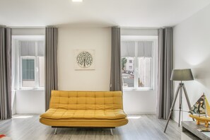 A modern living room with a sofa, a floor lamp, and a painting on the wall. - Tanoeiros Studio – 11 (Funchal)