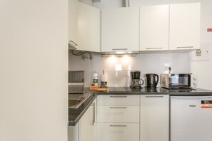 Een kleine keuken met witte kastjes, een ingebouwde magnetron, een koffiezetapparaat en een vaatwasser.