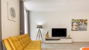 Un salon moderne avec un canapé, un téléviseur, une lampe et des œuvres d’art accrochées au mur.