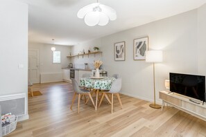 A modern living room with a dining area, a TV, and a kitchen in the background.
