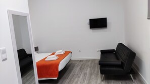 Una habitación de hotel con una cama, un televisor montado en la pared, un sofá de cuero negro y suelo de madera.