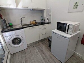 Uma cozinha compacta com máquina de lavar, micro-ondas e pia.