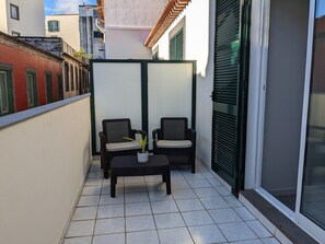 Un balcón con dos sillones de mimbre, una mesita y una planta en maceta.
