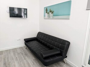 Un sofá negro con diseño acolchado, un televisor de pantalla plana montado en la pared y un cuadro con cactus.