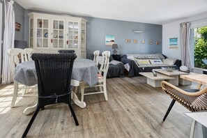 Een kamer met een eettafel, stoelen, een bank, een kast en een muur waarop het woord 'BEACH' staat.