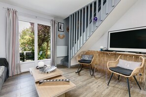 Een moderne woonkamer met een bank, een salontafel, rieten stoelen, een televisie en een trap.