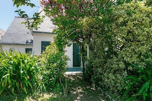 A garden pathway leading to a white building with a green door, surrounded by lush greenery and trees. - Sea View House "La Bastille" (La Turballe)