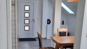A room with a wooden floor, a dining table with chairs, a door with frosted glass panels, and a hanging light fixture.