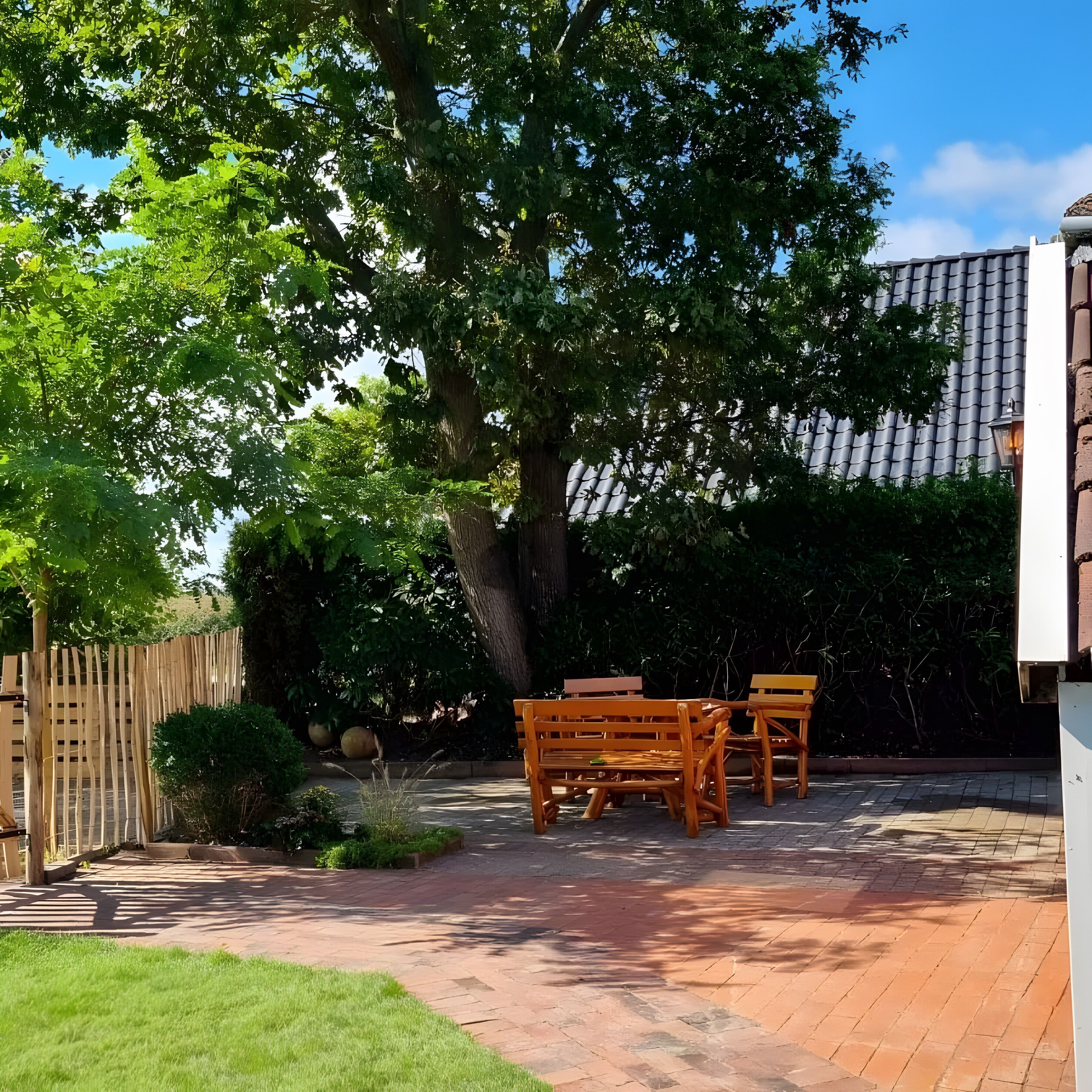 A patio with a wooden table and chairs, surrounded by a garden and a fence.
