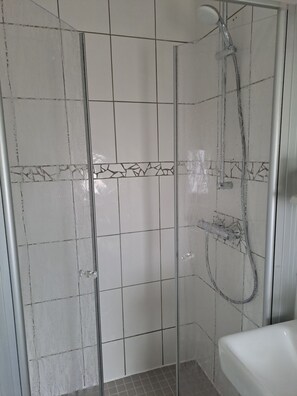 Área de duche com paredes em azulejo, chuveiro e mangueira de duche.