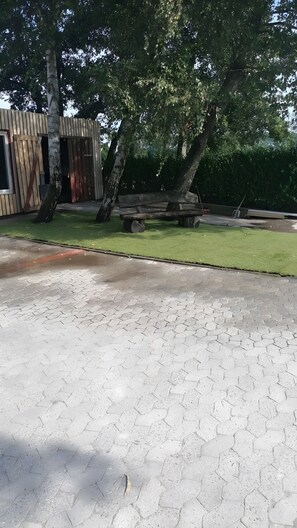 A paved walkway, a wooden structure with a red door, and a grassy area with trees. - Holiday Home 'Schwalbennest Vacation Home in The' with Wi-Fi (Dornum)