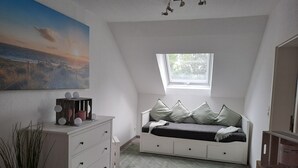 A bedroom with a sloped ceiling, a window, a bed with pillows, a dresser, and a painting on the wall.