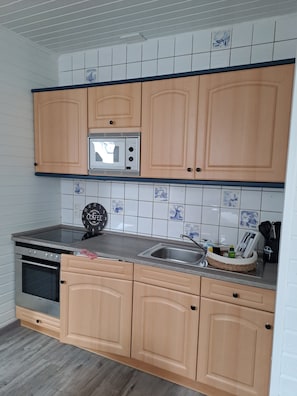 Uma cozinha com armários de madeira, micro-ondas, pia e relógio.