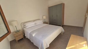 Quarto com cama, mesa de cabeceira, luminária, guarda-roupa e uma mesa de madeira.