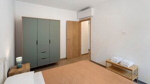 Un dormitorio con cama, armario, mesita de noche con lámpara y una pequeña mesa con toallas.