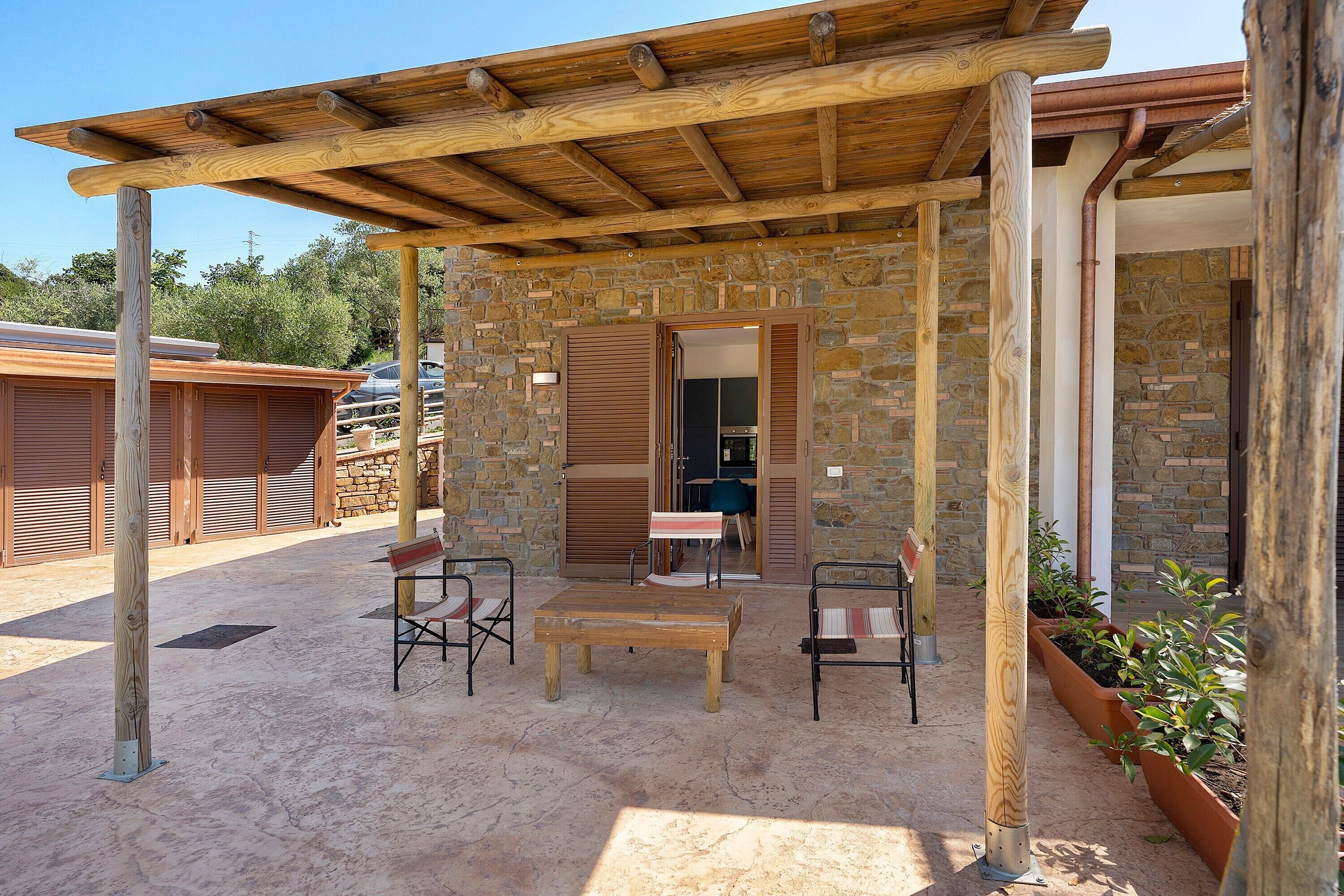 Ein überdachter Außenbereich mit Steinmauern, einer Holzpergola und Blick ins Gebäude.