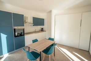 A modern kitchen with a wooden table and teal chairs, a built-in oven, and white cabinets.
