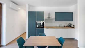 Cocina compacta con horno integrado, un lavamanos y cafetera. Hay una mesa de comedor con sillas.