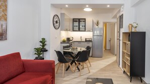 Un espacio habitable compacto con un sofá rojo, una mesa de comedor con sillas, una zona de cocina y una estantería.
