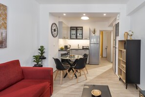 Un espacio habitable compacto con un sofá rojo, una mesa de comedor con sillas, una zona de cocina y una estantería.