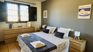 Ein Schlafzimmer mit Bett, Nachttischen, einem Schminktisch, einem Fenster und einem Wandbild.