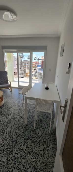Ein Zimmer mit einem weißen Tisch und Stühlen, einer Tür und einem Blick durch eine Glastür nach draußen.