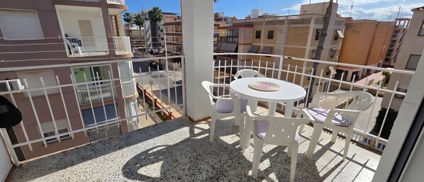 A balcony with a round table and chairs, a view of the street below, and a building with balconies.