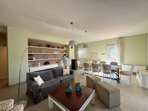 A living room with a sofa, coffee table, ottomans, and a dining area with chairs and a table.