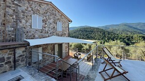 Un edificio de piedra con patio, asientos al aire libre y vistas a las montañas.