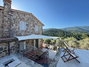 A stone building with a patio, outdoor seating, and a view of mountains.