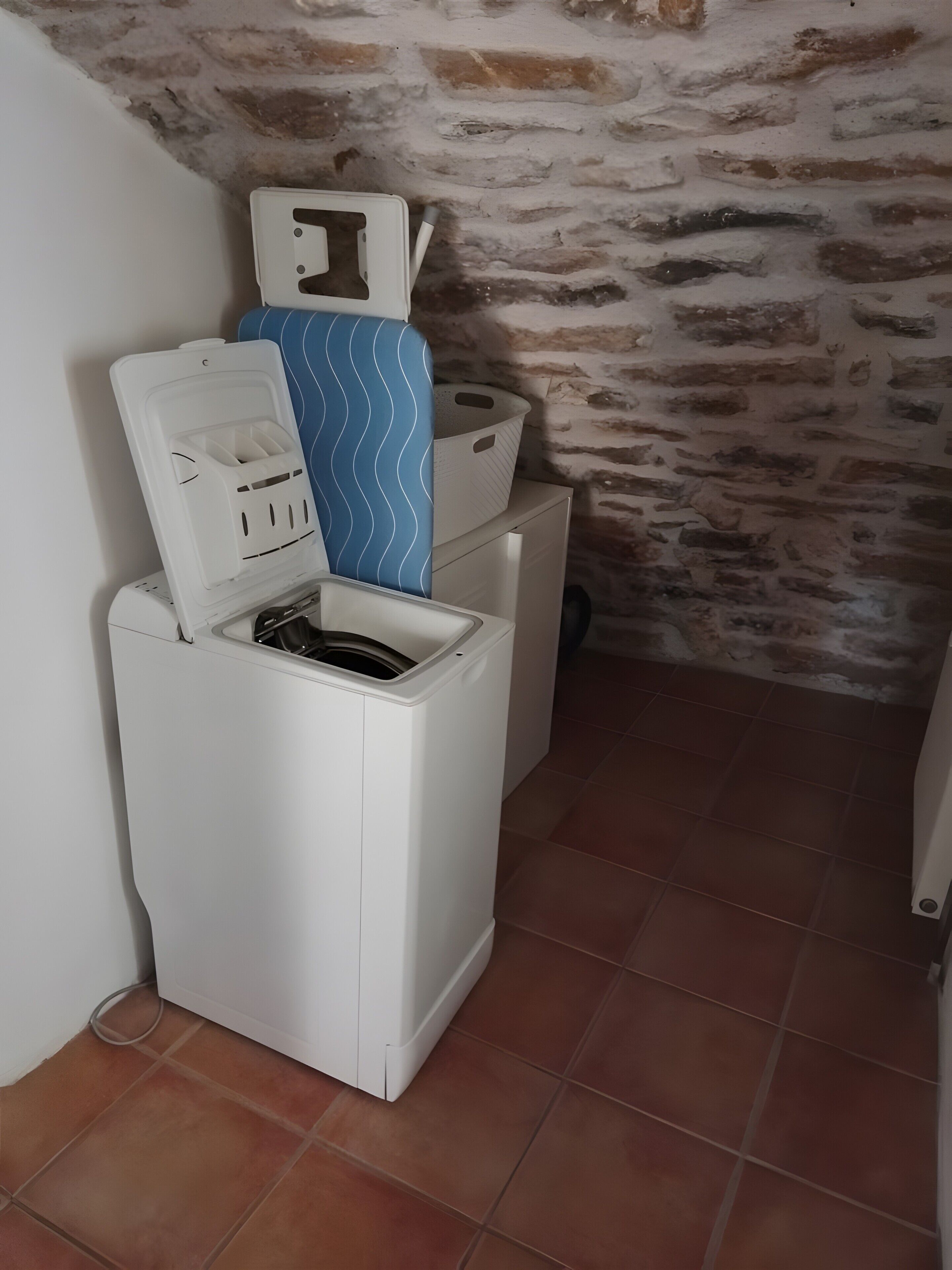 Une petite machine à laver blanche, dotée d’un couvercle bleu à motifs, d’un panier en plastique blanc et d’un récipient en plastique blanc placé sur le dessus.