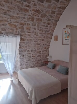 Un dormitorio con pared de piedra, una cama con cabecera rosa y un cuadro enmarcado en la pared.