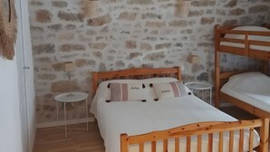 A bedroom with a wooden bed, a small bedside table, a lamp, and a stone wall. - Le gite de L' Alauzet – Charming Stone House with Panoramic Tarn Views (Paulhe)
