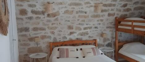 A bedroom with a wooden bed, a small bedside table, a lamp, and a stone wall.