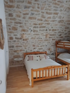 Ein Schlafzimmer mit einem hölzernen Bett, einem kleinen Nachttisch, einer Lampe und einer Steinwand.