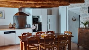 A kitchen with white cabinets, a stainless steel range hood, a microwave, a toaster, and a dishwasher. There is a wooden dining table with chairs. - Le gite de L' Alauzet – Charming Stone House with Panoramic Tarn Views (Paulhe)
