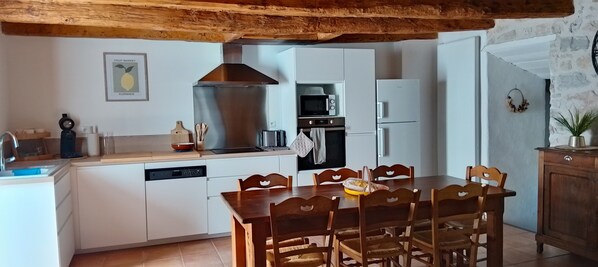 Eine Küche mit weißen Schränken, einer Edelstahl-Dunstabzugshaube, einer Mikrowelle, einem Toaster und einem Geschirrspüler. Es gibt einen Holztisch mit Stühlen.