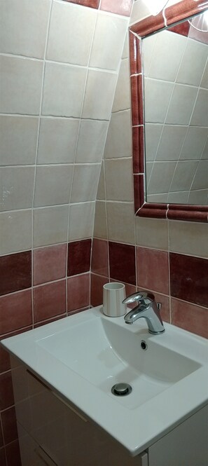 Ein Badezimmer mit einem weißen Waschbecken, einem Spiegel und roten und weißen Fliesen.