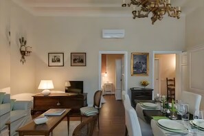 Une salle à manger avec une longue table dressée pour le repas, un lustre et des tableaux encadrés accrochés au mur.