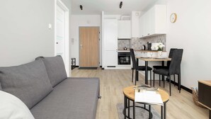 Un appartamento moderno con un divano grigio, un tavolo da pranzo con sedie, un angolo cottura e una porta in legno.