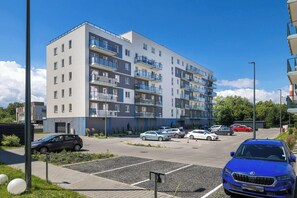 Ein mehrstöckiges Wohngebäude mit Balkonen, ein Parkplatz mit mehreren Autos und ein klarer Himmel.